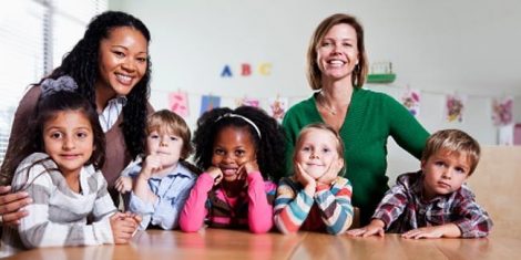 Two teachers stand behind a row of smiling children